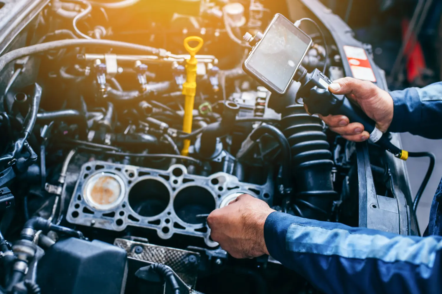 Hände eines Automechanikers prüfen den Fahrzeugmotor mit technischem Endoskop mit rotierender Kamera und Mobiltelefon.